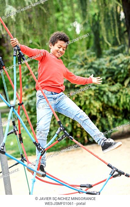 Little boy playing on playground in a park, climbing in a jungle gym