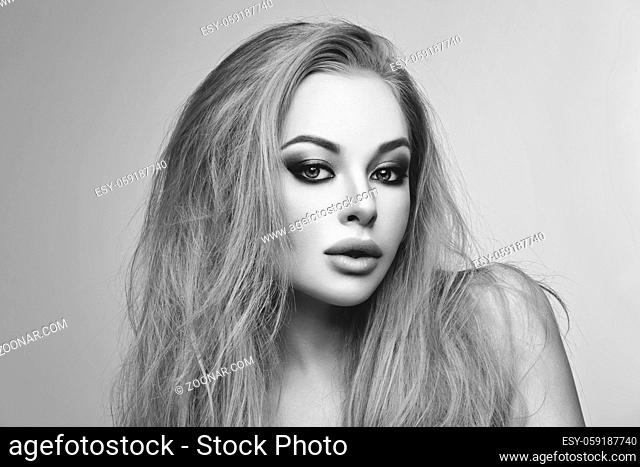 Closeup portrait of beautiful young woman with messy long blond hair and bright makeup. Beauty shot over grey background