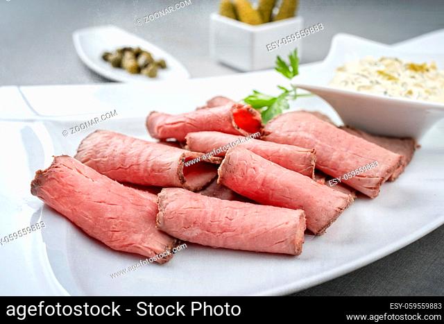 Traditional lunch meat with sliced cold cuts roast beef and remoulade as closeup on a white plate