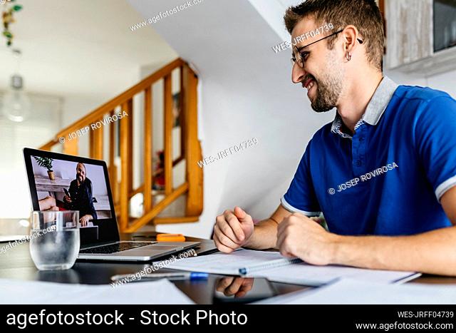 Smiling man consulting professor through video call from laptop at home