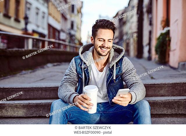 Man with coffee sitting on stairs in the city using phone