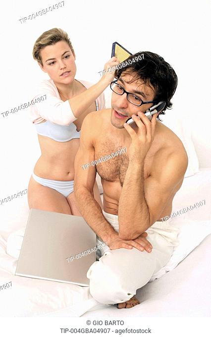 Couple sitting on bed, man on mobile