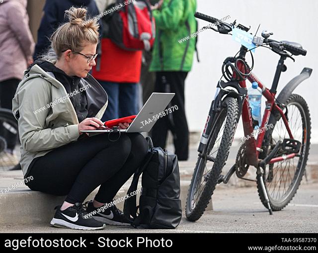 RUSSIA, ST PETERSBURG - JUNE 3, 2023: Una mujer utiliza un portátil antes del paseo en bicicleta de masa ZSD Fontanka Fest a lo largo de la carretera de...