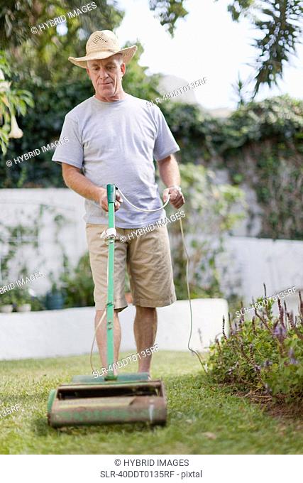Older man mowing lawn in backyard
