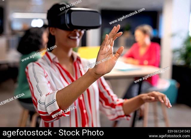 Young biracial businesswoman experiencing virtual reality simulator while gesturing at workplace