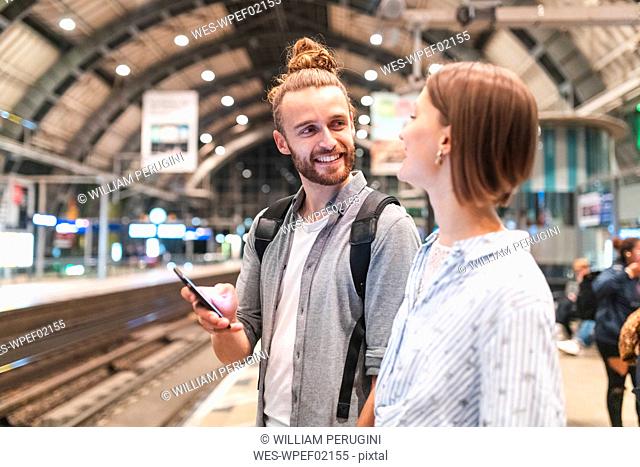 Young couple waiting for the train at the station and using smartphone, Berlin, Germany
