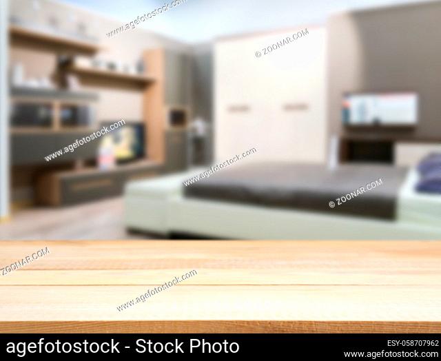Wooden board empty table in front of blurred background. Perspective light wood over blur in modern comfortable bedroom with white bed