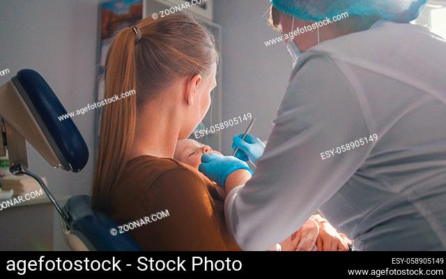 Dentist examining and consulting the daughter sitting on her mother knees, health care since childhood