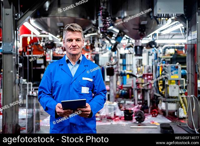 Mature engineer holding digital tablet while standing in industry