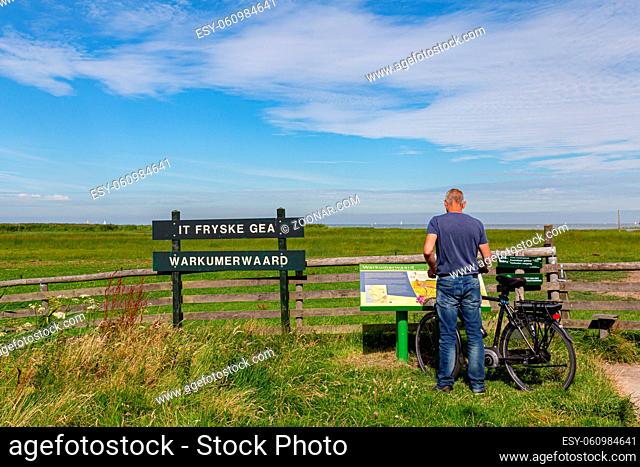 Workum, Netherlands - August 6, 2020: Male tourist reading information sign at entrance of nature reserve Warkumerwaard along IJsselmeer Netherlands