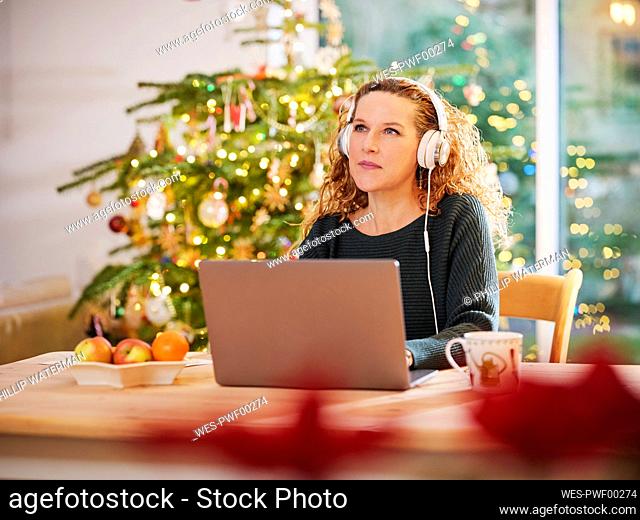 Woman with headphones looking away while sitting in front of laptop at Christmas