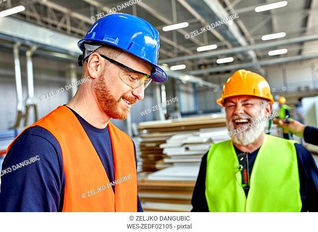 Happy colleagues in protective workwear talking in factory
