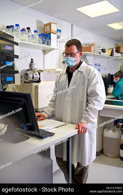Male scientist in face mask using computer in laboratory