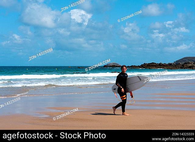 Sables D Or Les Pins, Bretagne / France - 20 August 2019: Young surfer walking on the beach after a fun surfing session in the waves on the coast of Brittany in...