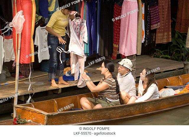 Female tourist in a wooden boat choosing a dress at a stand at Floating Market, Damnoen Saduak, near Bangkok, Ratchaburi, Thailand