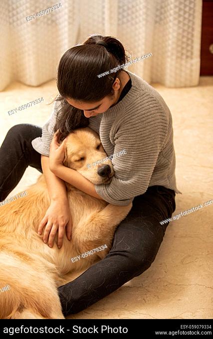 A YOUNG GIRL SITTING AND CUDDLING PET DOG