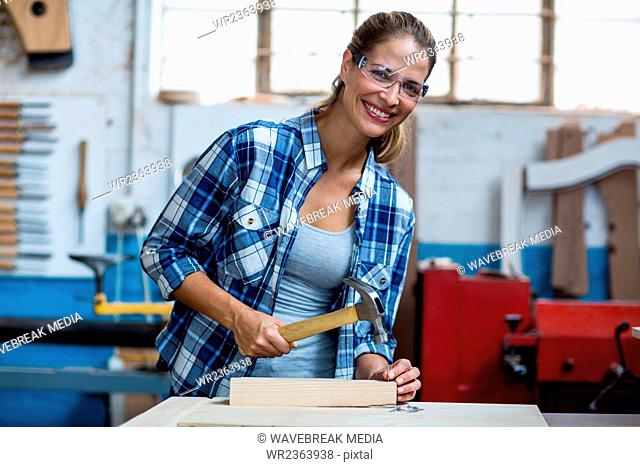 Female carpenter holding a hammer to drive nail into a wooden plank