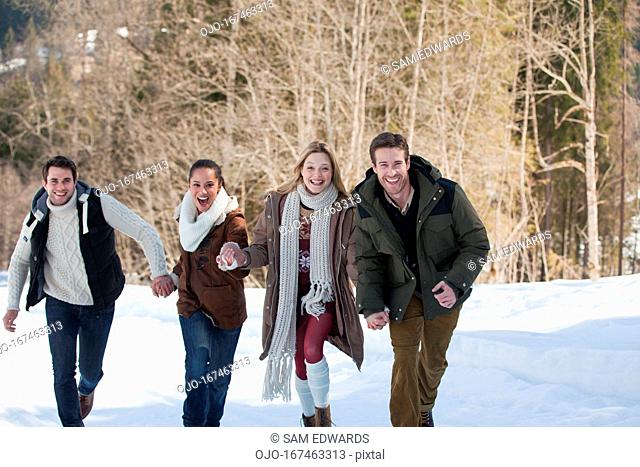 Portrait of smiling friends holding hands and running in snow