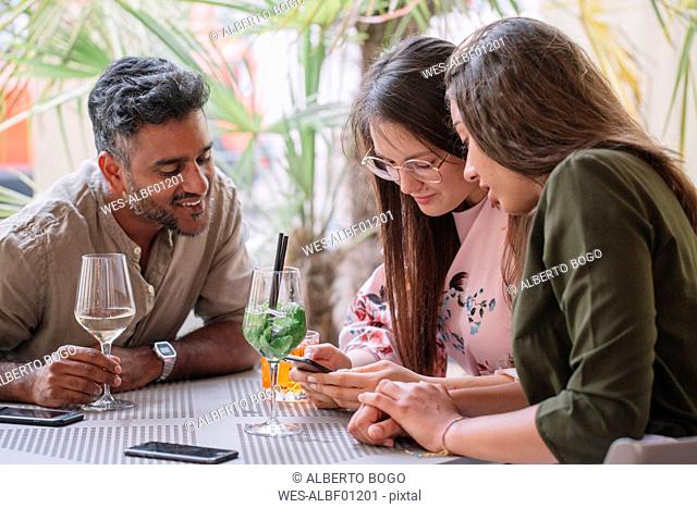 Friends sitting at table with drinks looking at smartphone
