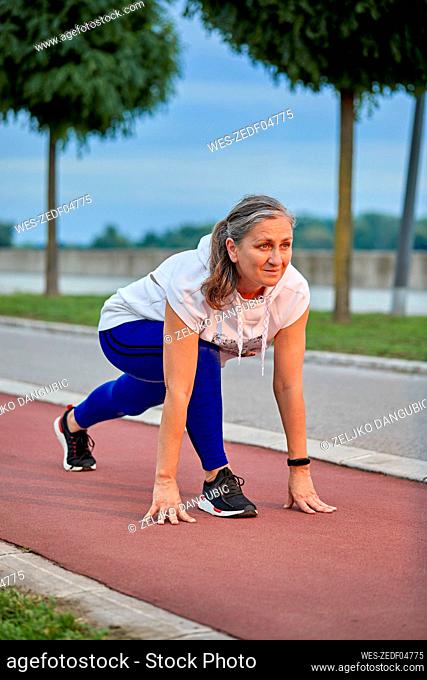Smiling mature woman preparing for run at sports track