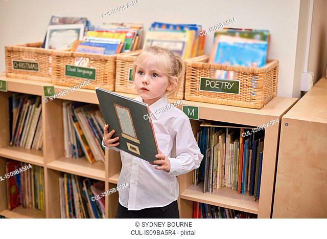 Cute schoolgirl holding book in classroom at primary school