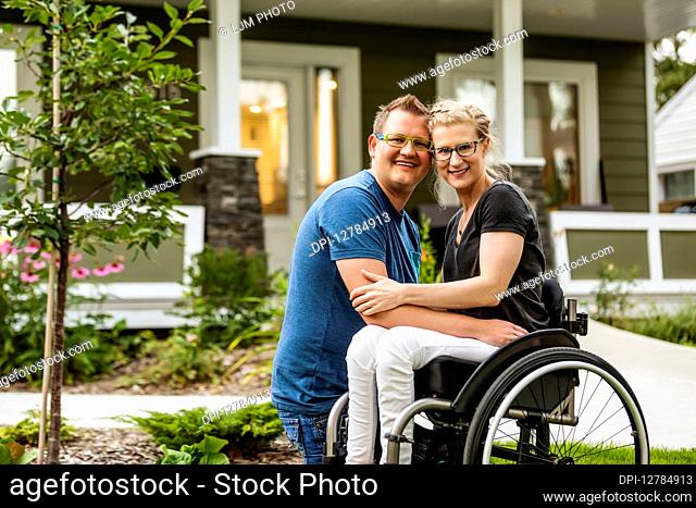 A husband and his paraplegic wife posing for a family photo in their front yard on a warm fall day: Edmonton, Alberta, Canada