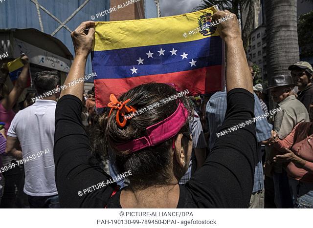 30 January 2019, Venezuela, Caracas: A woman is holding up a Venezuelan flag in a protest against the government of Head of State Maduro