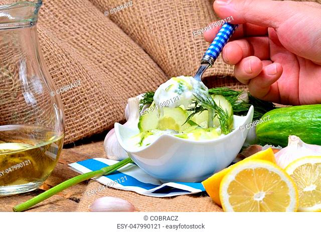 Man eating Tzatziki - traditional Greek dressing or dip sauce, garlic, lemon, dill, cucumber, jug with oil, blue spoon and decoration in background
