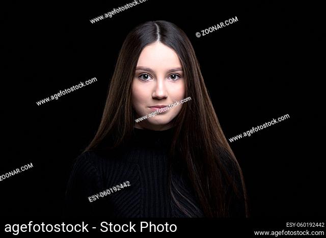 Beautiful girl with dark long hair on a black background. Seventeen-year-old woman. Proper facial features