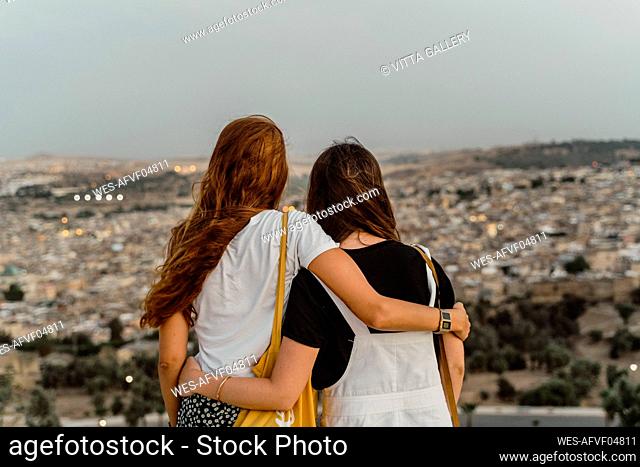Back view of two best friends enjoying city view arm in arm in the evening, Fez, Morocco