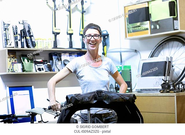 Woman in workshop holding recumbent bicycle looking at camera smiling