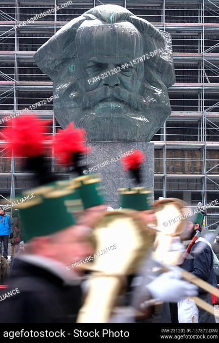 02 December 2023, Saxony, Chemnitz: Participants in a mining parade walk past the Karl Marx Monument. On the eve of the first Advent