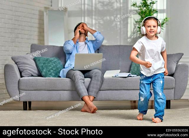 cute little child girl dancing and unhappy busy dad working with laptop at home