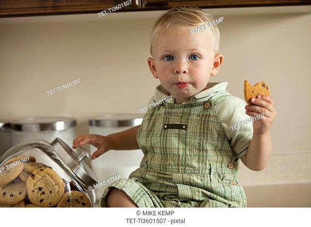 Portrait of baby boy 12-17 months holding cookie in kitchen