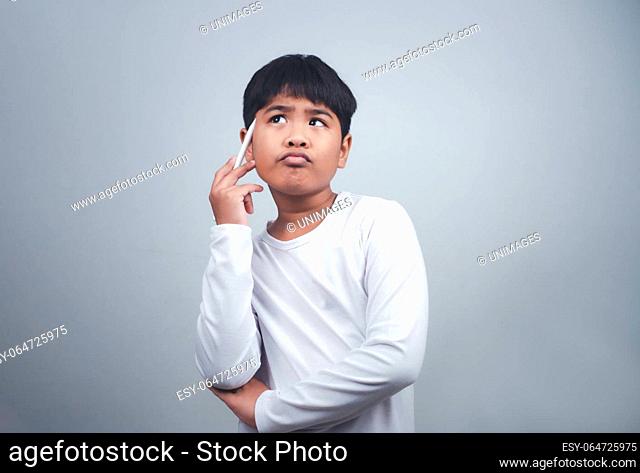 A boy in a white shirt is holding a white pen on a white background. Shows thinking, pondering, and considering options