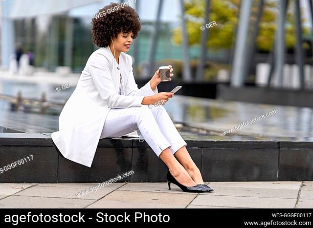 Businesswoman drinking coffee while using mobile phone outdoors