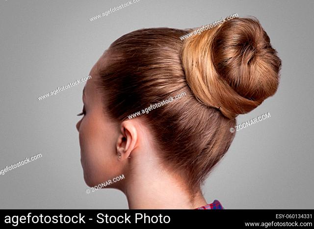 Profile side view closeup portrait of woman with creative elegant brown collected hairstyle, bun hair. indoor studio shot, isolated on grey background