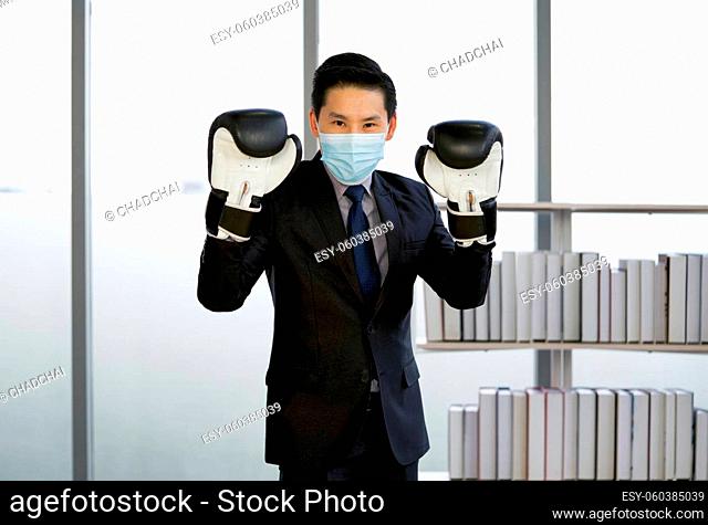 Asian businessman dressed in suit and necktie, wearing a face mask and a boxing glove. Standing posture ready for boxing