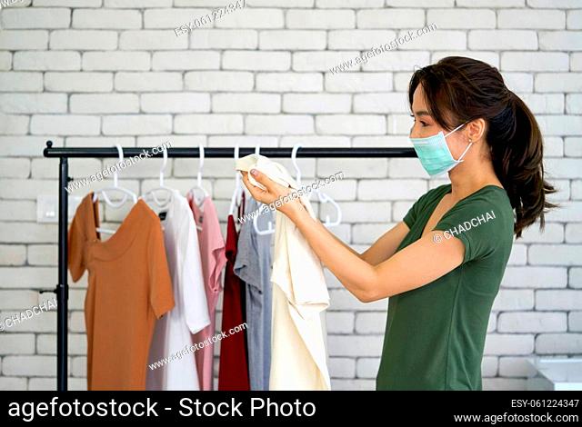Young asian laundry worker wearing face mask while looking at the cloth before hanging. Working atmosphere in the laundry room