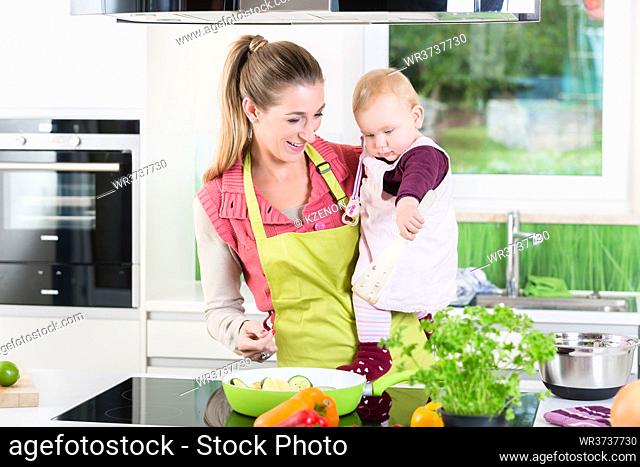 Mum cooking food with baby in arm