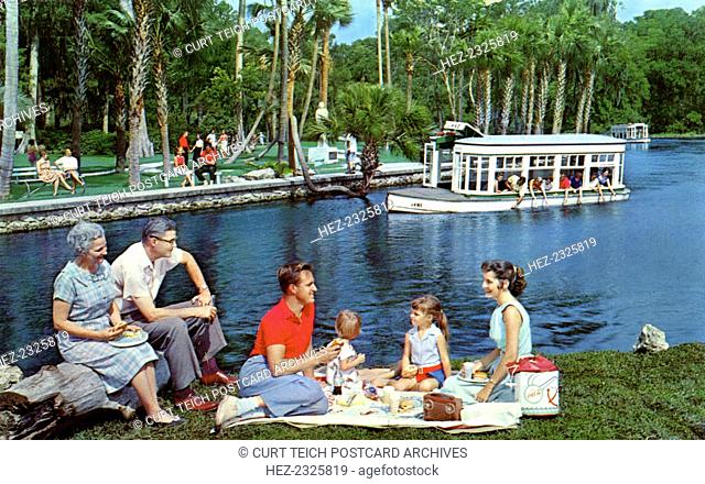 A family having a picnic beside the water, Silver Springs, Florida, USA, 1959. A glass bottomed boat is in the background