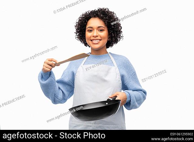 smiling woman in apron cooking food in frying pan