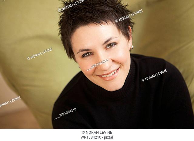 A woman with short spiky brown hair, wearing a black turtleneck sweater. Smiling and looking up