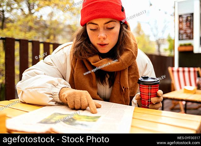 Woman with coffee cup reading newspaper while sitting at sidewalk cafe