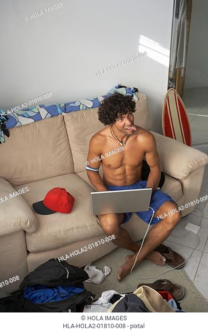 High angle view of a young man sticking his tongue out and using a laptop
