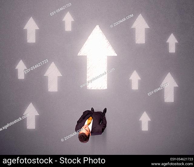 Young contemplating businessman stands in front of white arrows