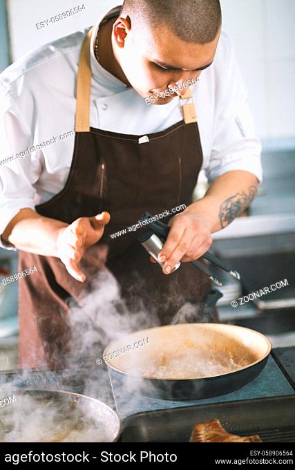 Young attractive male cook with uniform preparing a meat sause. The figure in a bent form