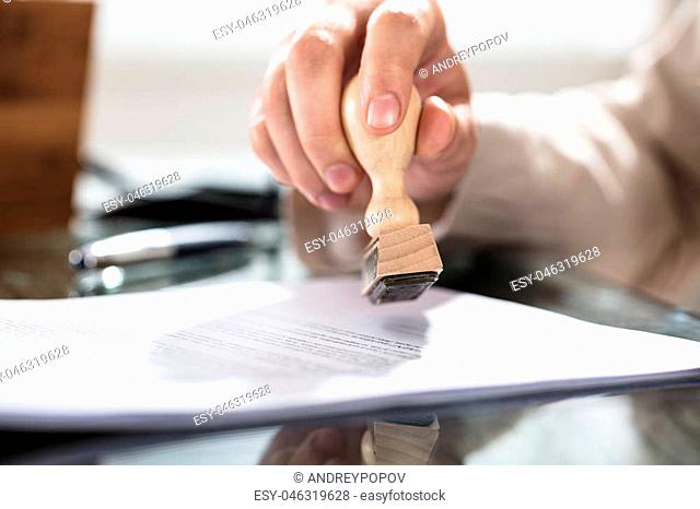 Close-up Of A Person's Hand Stamping On Approved Application Form Over The Desk