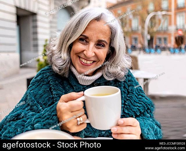 Happy senior woman with coffee cup sitting in sidewalk cafe