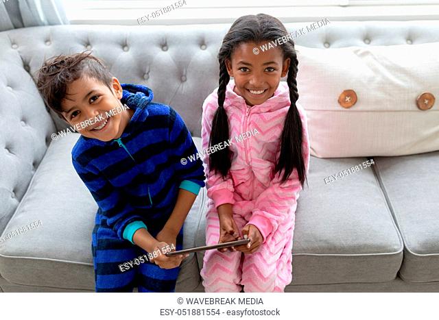 Siblings using digital tablet on a sofa in living room at home